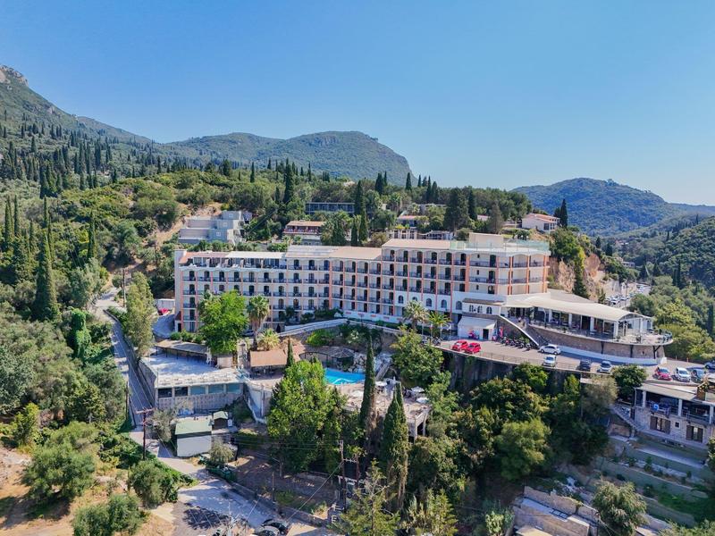 Een groot hotel met zwembad, omgeven door groene heuvels en bergen onder een heldere lucht.