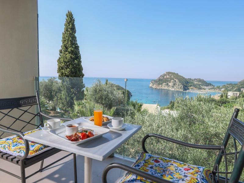 Balkon met twee stoelen, tafel met ontbijt, uitzicht op zee en eiland bij heldere lucht.