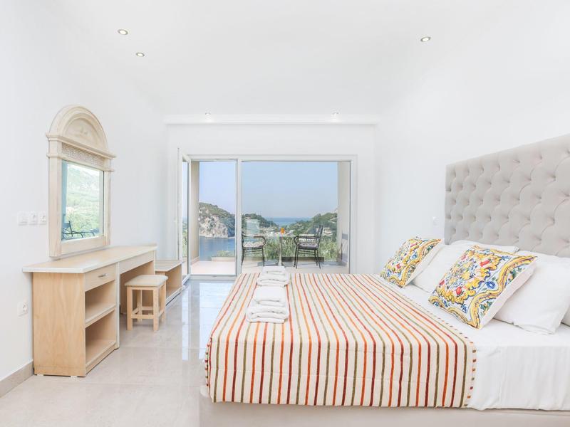 Lichte, moderne slaapkamer met groot bed, bureau en uitzicht op tuin en zwembad.