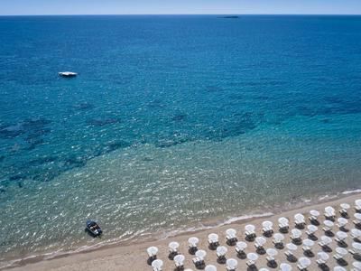 Mare turchese chiaro con spiaggia di sabbia bianca e file di ombrelloni.
