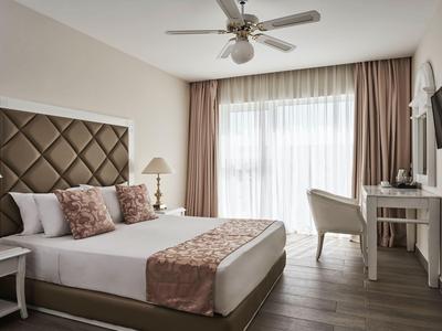 Habitación de hotel luminosa con cama grande, escritorio, silla y grandes cortinas en la ventana.