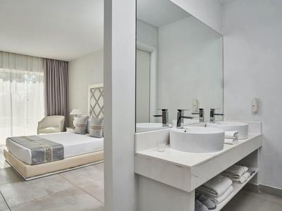 Camera d'hotel moderna con bagno aperto, letto matrimoniale e grandi finestre con tende.