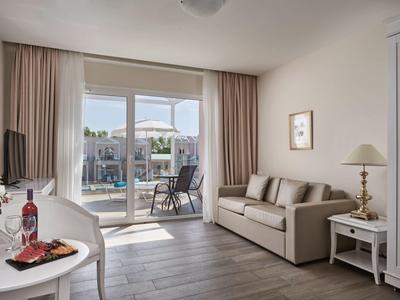 Soggiorno luminoso con divano, tavolo, TV e accesso alla terrazza con vista piscina.