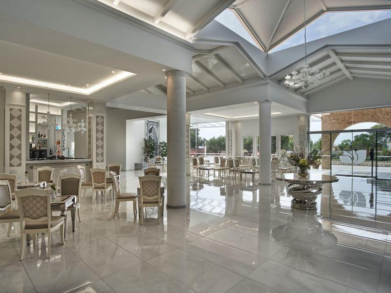 Hall dell'hotel luminoso con arredi moderni, sedie bianche e ampia finestra panoramica.