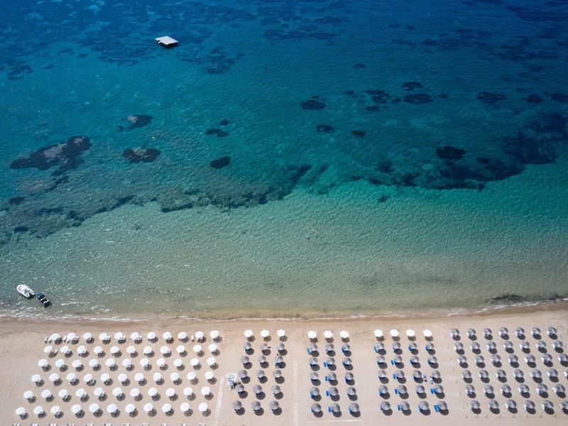 Spiaggia con file di ombrelloni e acqua azzurra limpida sullo sfondo.