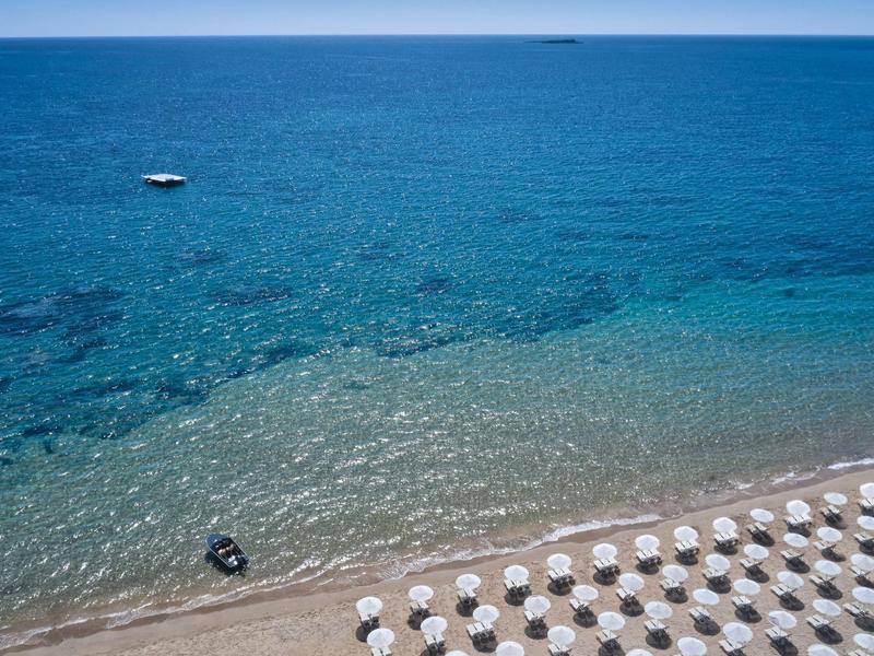 Mare turchese chiaro con spiaggia di sabbia bianca e file di ombrelloni.