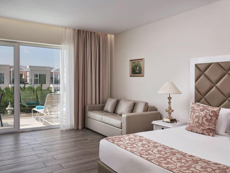 Camera d'albergo elegante con letto, divano e accesso a una terrazza con vista sulla piscina.
