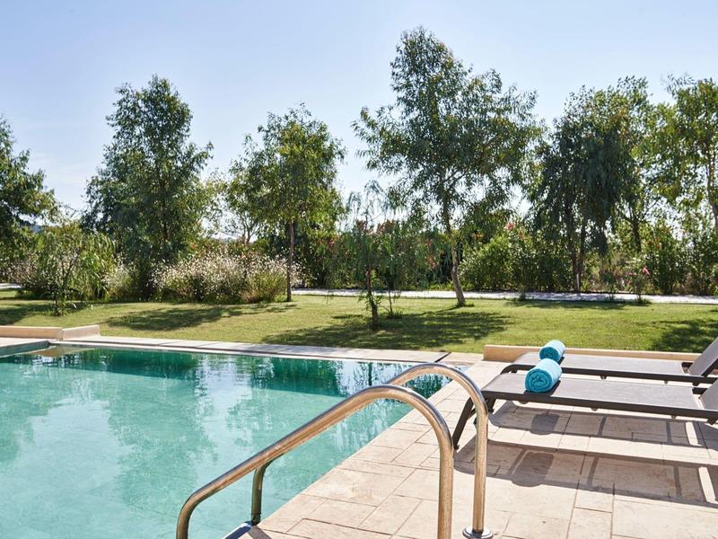 Piscina con lettini e alberi sullo sfondo in un giardino soleggiato.