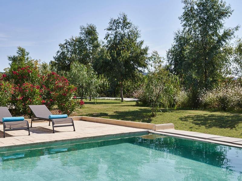 Superficie d'acqua chiara della piscina con lettini sulla terrazza e giardino verde sullo sfondo.