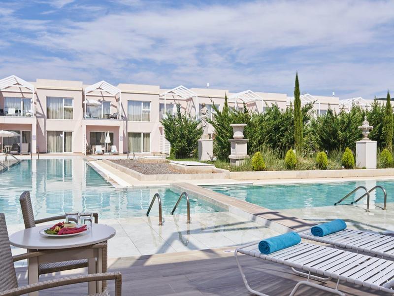 Area piscina con lettini e camere d'hotel moderne sullo sfondo sotto un cielo limpido.