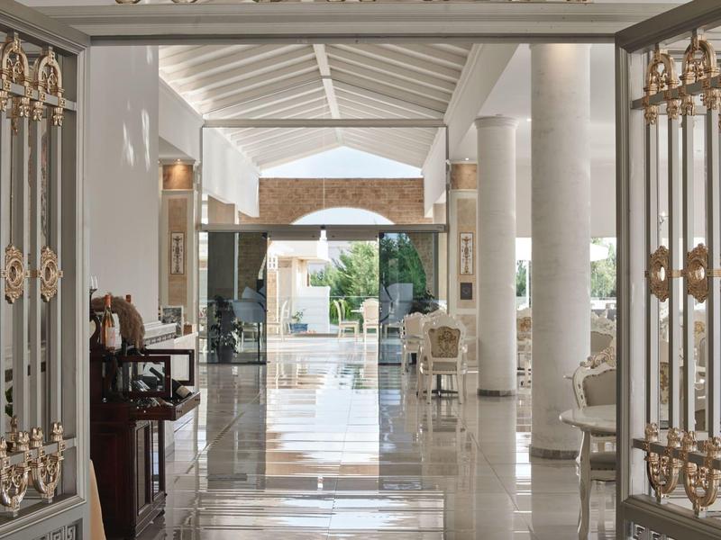 Ingresso luminoso della hall dell'hotel con pavimento in marmo, cancelli decorativi e aree salotto.