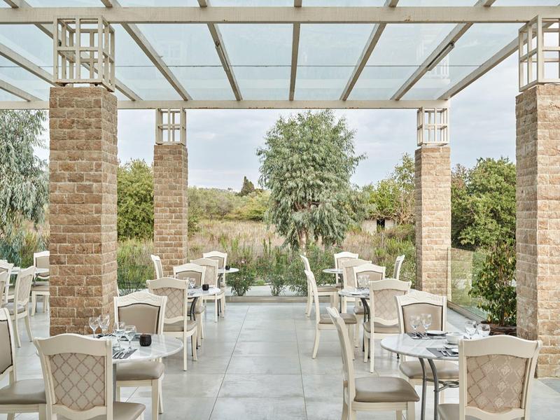 Area terrazza aperta dell'hotel con sedie e tavoli bianchi, circondata da verde.