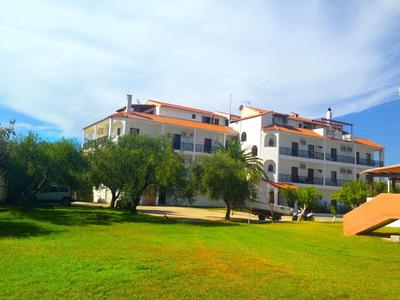 Modernes Hotel mit Terrassen, umgeben von grünem Rasen und Bäumen unter bewölktem Himmel.