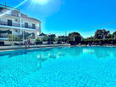 Großer klarer Hotelpool mit weißen Sonnenschirmen und einer dreistöckigen Unterkunft im Hintergrund.