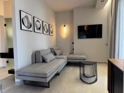 Modern eingerichtetes Hotelzimmer mit grauer Eckcouch, Wandkunst und Flachbildfernseher.