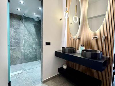 Modernes Badezimmer mit grauem Boden, Holzpaneelen und zwei ovalen Spiegeln.