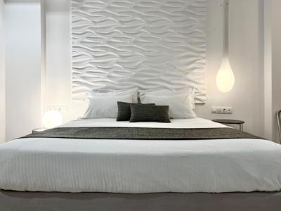 Modernes Hotelzimmer mit großem Bett vor einer wellenförmigen weißen Wand und hängender Lampe.
