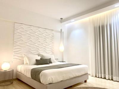 Modern eingerichtetes Hotelzimmer mit großem Bett, dekorativen Kissen und Vorhängen.