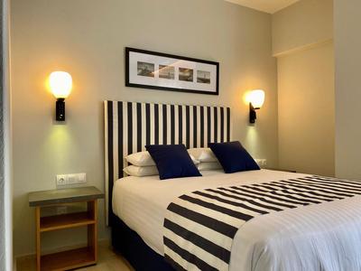 Modernes Hotelzimmer mit Bett, gestreiften Bettwäsche, blauen Kissen und zwei Wandlampen.