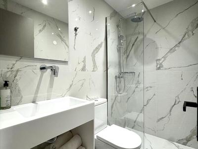 Modernes weißes Badezimmer mit Marmorfliesen und Glasdusche in Hotelambiente.