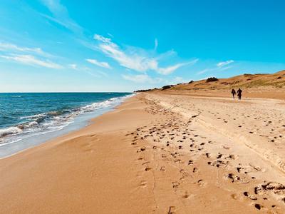 Ein weiter Sandstrand mit Fußspuren und zwei Menschen am Horizont bei klarem Himmel.