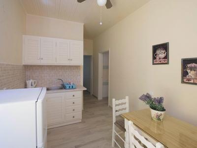 Kleine Küche mit weißen Möbeln, hellem Holztisch, zwei Stühlen und Wandbildern.