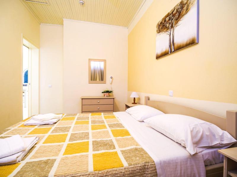 Hell eingerichtetes Schlafzimmer mit gelb kariertem Bettüberwurf, hellen Wänden und Holzdecke.