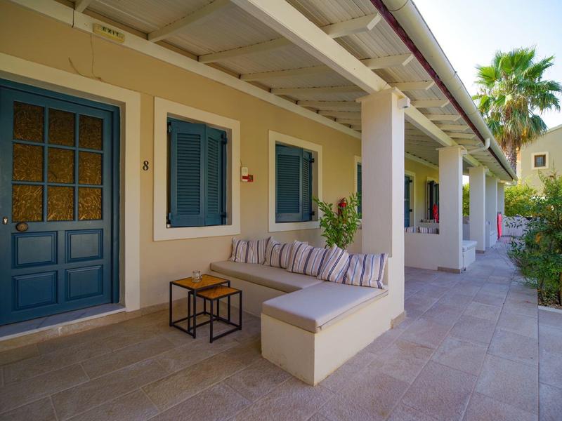 Hausfassade mit blauen Türen, Fenstern, grauem Sofa, Holztisch und Palmen im Hintergrund.
