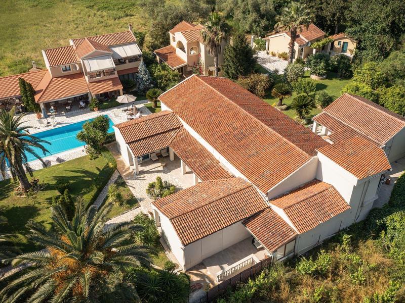 Großes Landhaus mit rotem Ziegeldach, umgeben von Bäumen, Pool und Grünflächen.