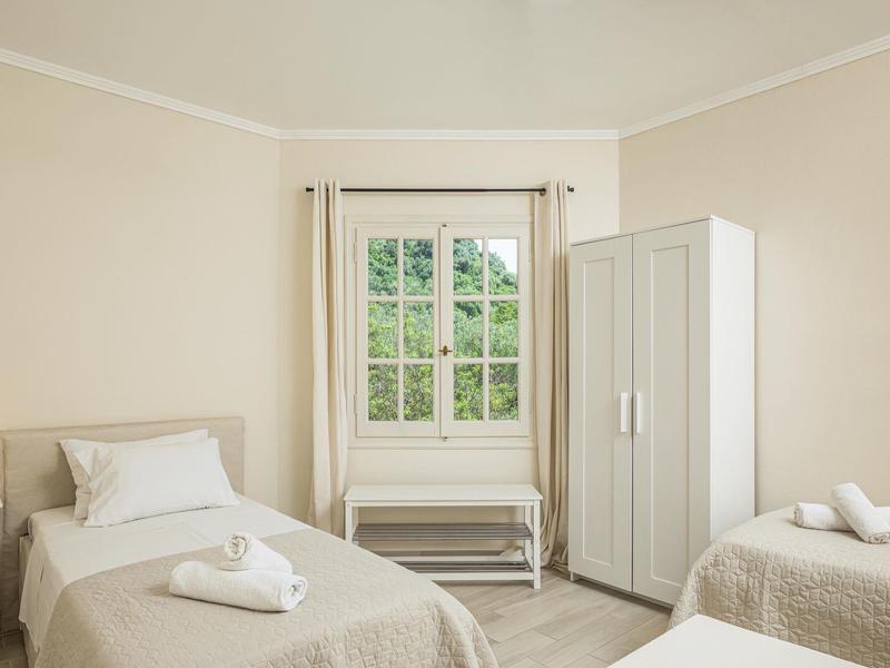 Hell eingerichtetes Zimmer mit zwei Einzelbetten, weißem Schrank, Nachttisch und Fenster mit Blick ins Grüne.