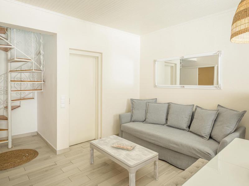 Ein heller, schlichter Wohnraum mit grauem Sofa, kleinem Couchtisch und weißer Wendeltreppe.