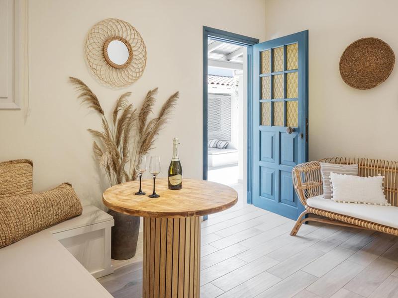 Helles Wohnzimmer mit blauem Türrahmen, runder Holzsäulentisch, Rattansofa und Wanddekoration.