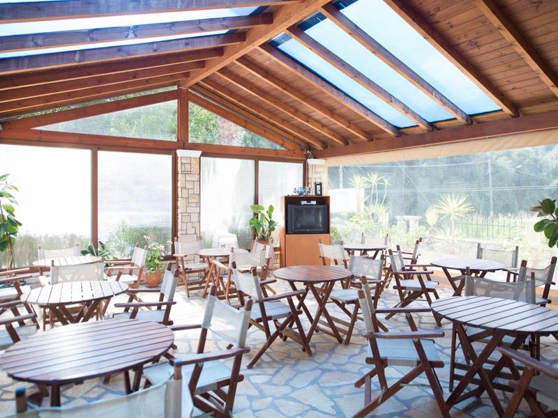 Hell eingerichteter Wintergarten mit Holztischen und Stühlen, großen Fenstern und Pflanzen.