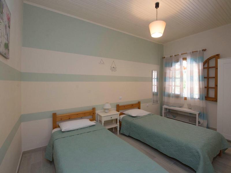 Kleines Schlafzimmer mit zwei Einzelbetten, hellgrünen Wänden und Fenster mit gemusterter Gardine.