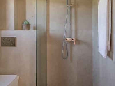 Modernes Badezimmer mit beiger Dusche, Glaswand, Wand-WC und weißen Handtüchern.
