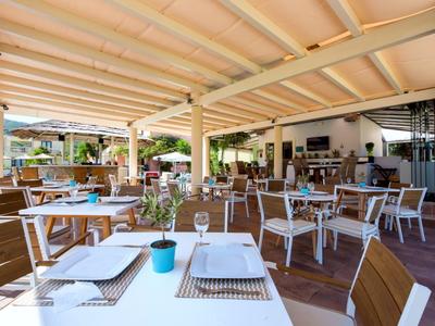 Zastřešená venkovní terasa s prostřenými stoly a židlemi v hotelové restauraci.
