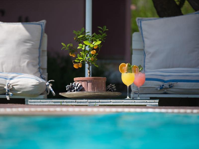 Twee loungestoelen met kussens naast een klein tafeltje met een plant en twee kleurrijke cocktails bij het zwembad