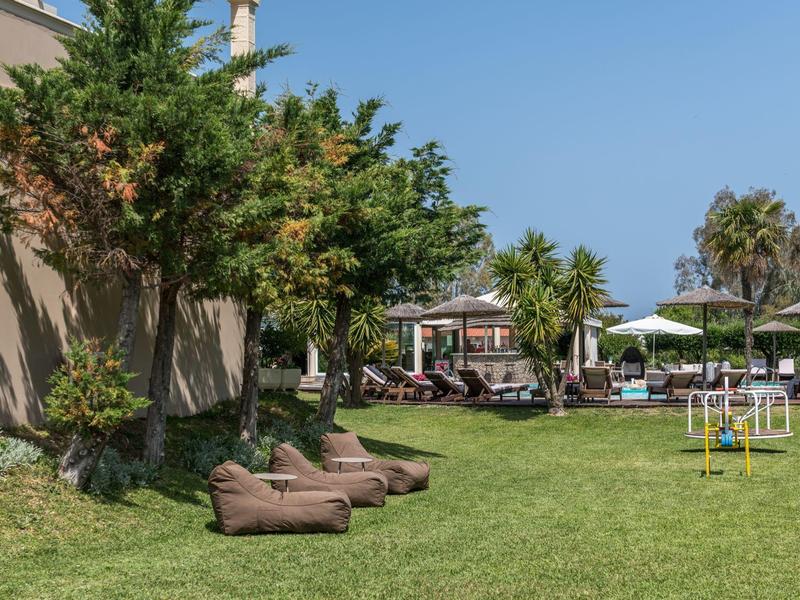 Groen tuingebied met ligstoelen en schaduwrijke parasols voor een hotel.