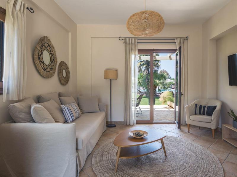 Gezellige woonkamer met bank, ronde vloerkleed en uitzicht op tuin via glazen deur.