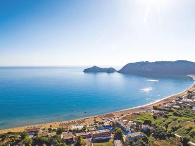 Widok z powietrza na długą piaszczystą plażę obok nadmorskiego miasta z górami w tle.