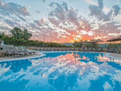 Piscine d'hôtel au coucher du soleil avec transats et reflets de nuages dans l'eau.