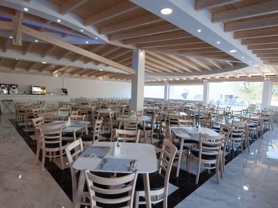 Grande salle à manger moderne avec de nombreuses tables et chaises sous un plafond à poutres en bois.