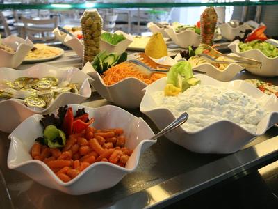 Bufet z różnymi sałatkami i świeżymi składnikami w białych misach.