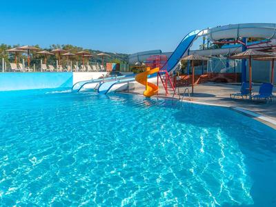 Duży basen z zjeżdżalniami wodnymi i czystą, niebieską wodą pod błękitnym niebem.