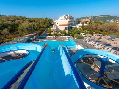 Parc aquatique avec toboggans bleus et jacuzzis dans une zone hôtelière avec des transats.