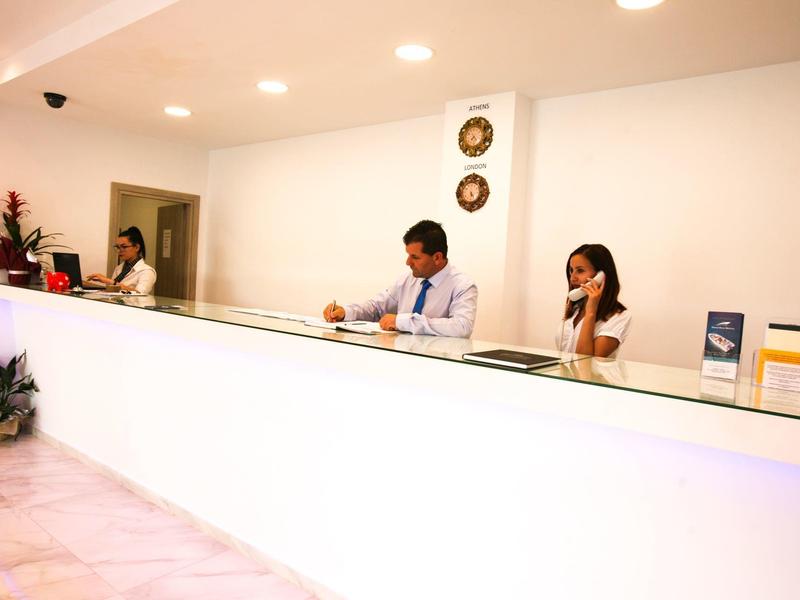 Trzech recepcjonistów pracuje przy białej recepcji w jasnym biurze hotelowym.