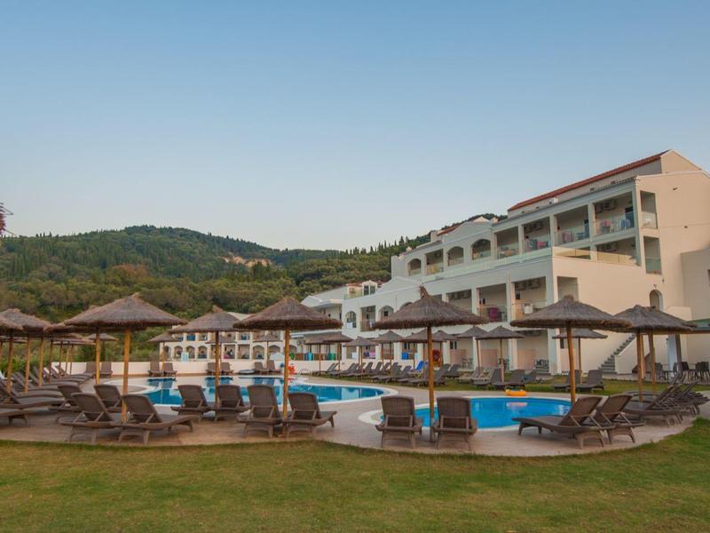 Ośrodek hotelowy z basenem, leżakami i parasolami przed zalesionymi wzgórzami pod czystym niebem.