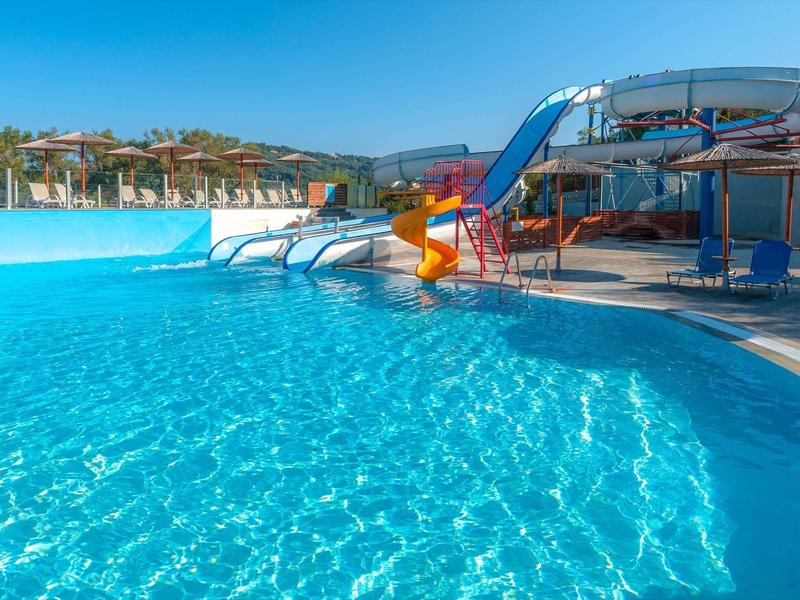 Duży basen z zjeżdżalniami wodnymi i czystą, niebieską wodą pod błękitnym niebem.