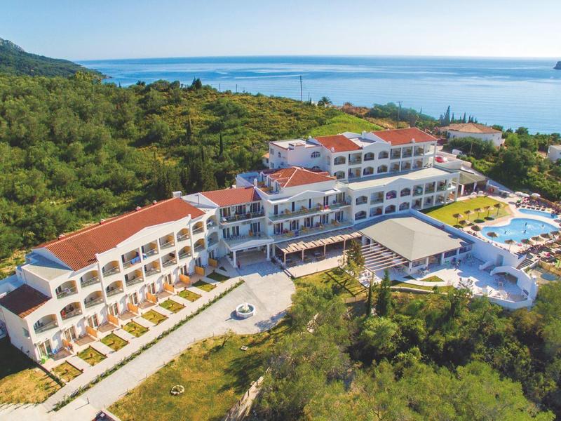 Duży hotel z basenami blisko wybrzeża i zalesionego terenu pod jasnym niebem.