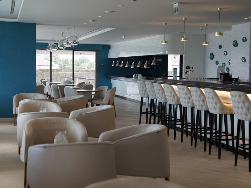 Moderne hotel lounge met beige fauteuils en een hoge bar met krukken onder hanglampen.